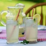 two glasses of lemonade with a pitcher of lemonade on a table