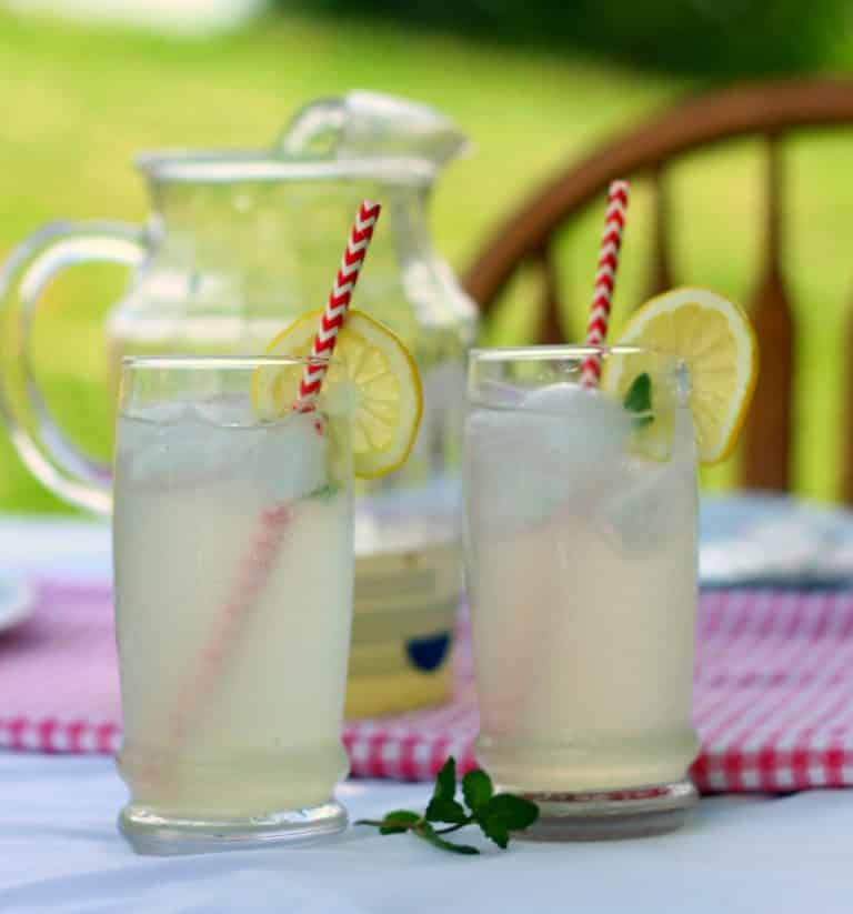 two glasses of lemonade with a pitcher of lemonade on a table