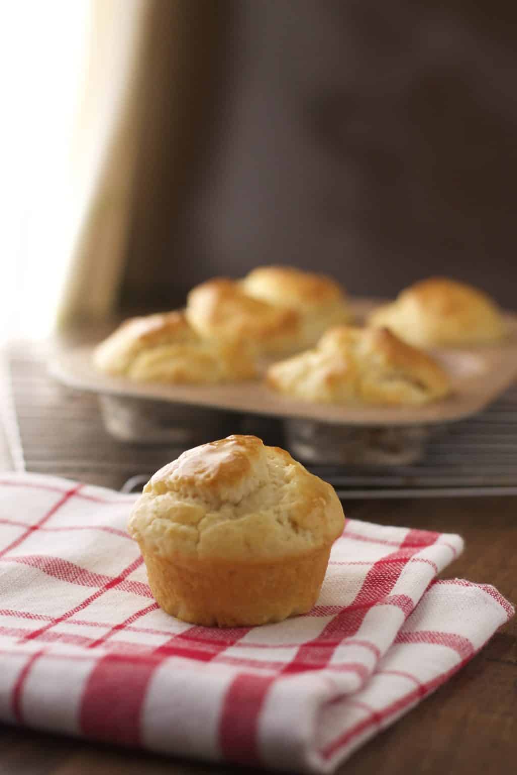 one dinner roll on a red napkin and a muffin tin with other dinner rolls in the background