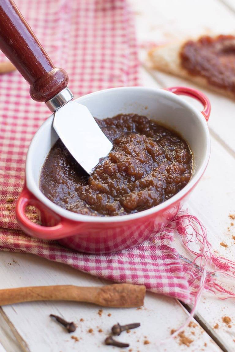 a bowl of apple butter with a red knife inside on a red plaid napkin