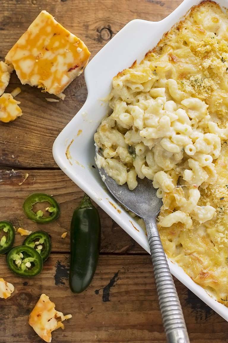 a baking dish of macaroni and cheese with sliced jalapenos and a block of cheese on the side