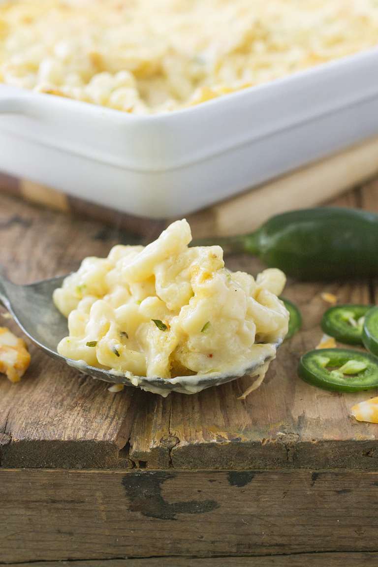 a spoonful of macaroni and cheese with sliced jalapenos on the side on a wooden table