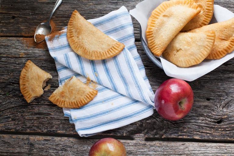 a view of a pan of apple pies and one broken open on a blue napkin with an apple