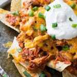a pile of chicken nachos on a plate with sour cream and green onions