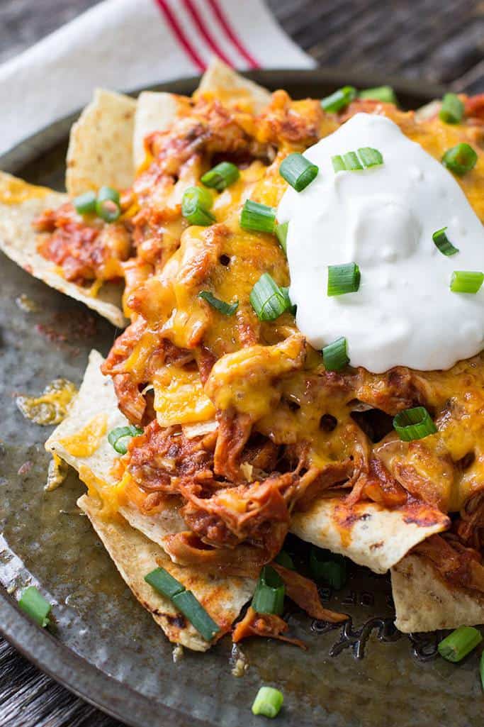 a pile of chicken nachos on a plate with sour cream and green onions