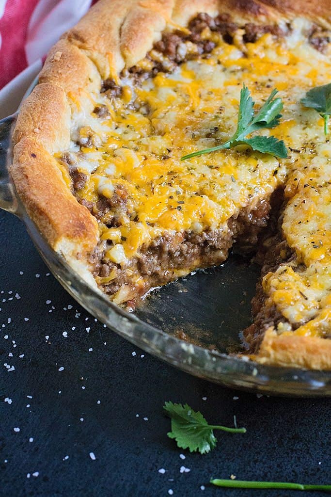 a taco pie in a glass baking dish with a slice out to show the beef filling