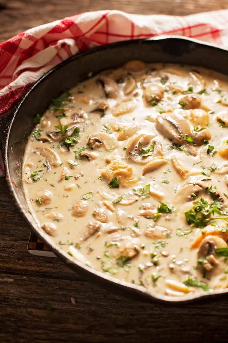 a skillet of chicken in cream sauce on a table with a red plaid napkin 