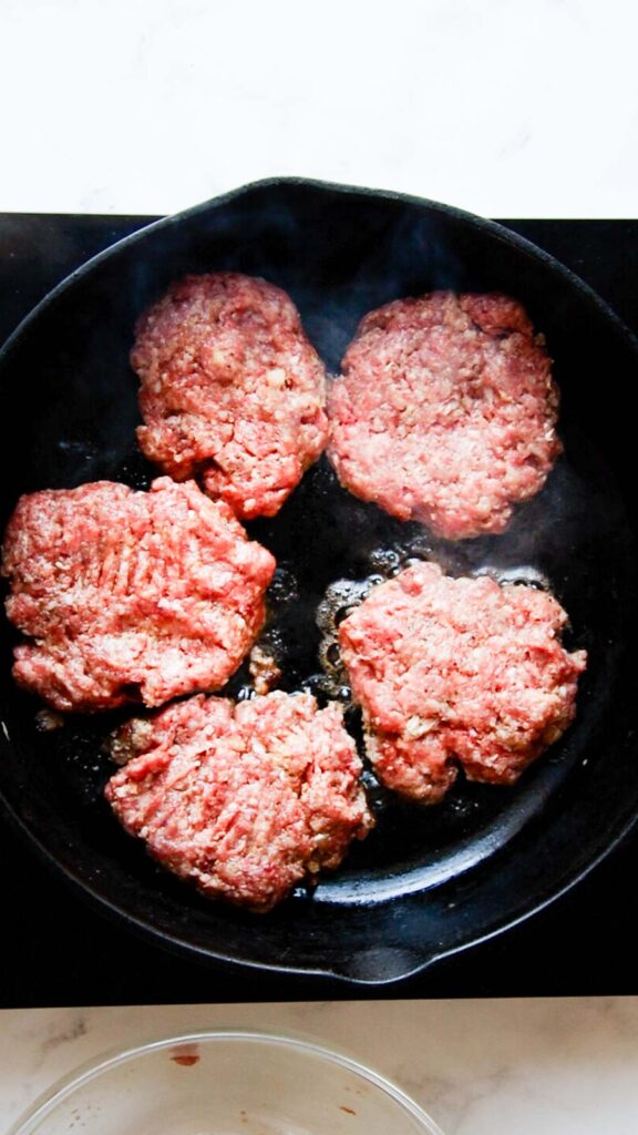 a skillet with five hamburger steak patties cooking