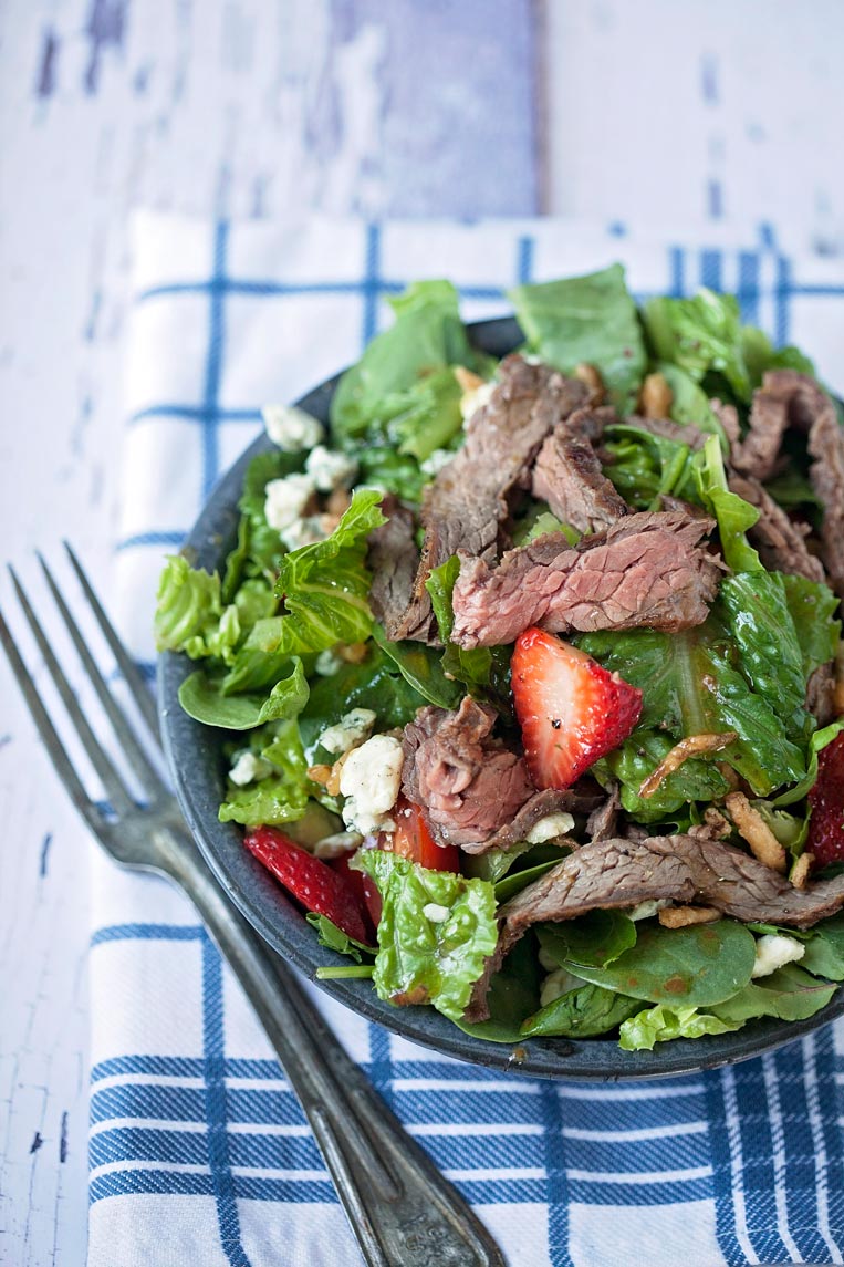 a bowl of steak salad with a fork on a blue napkin