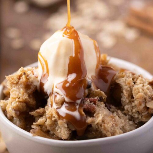 a bowl of apple pear crisp with ice cream on top and a drizzle of caramel being added