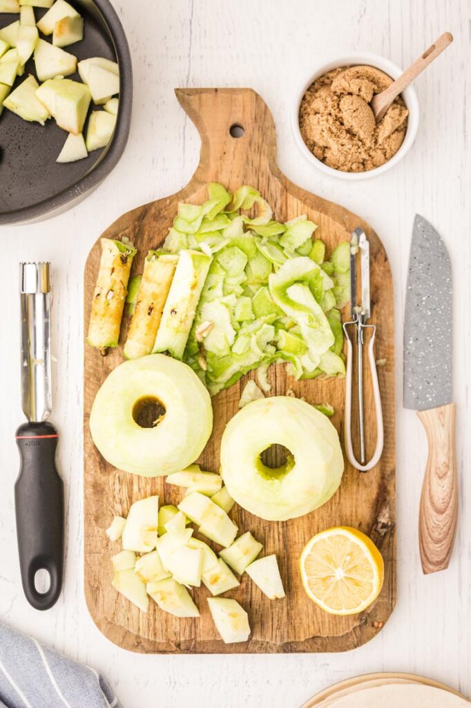 apples cut and cored on a cutting board with peels laying around them with a knife and peeler