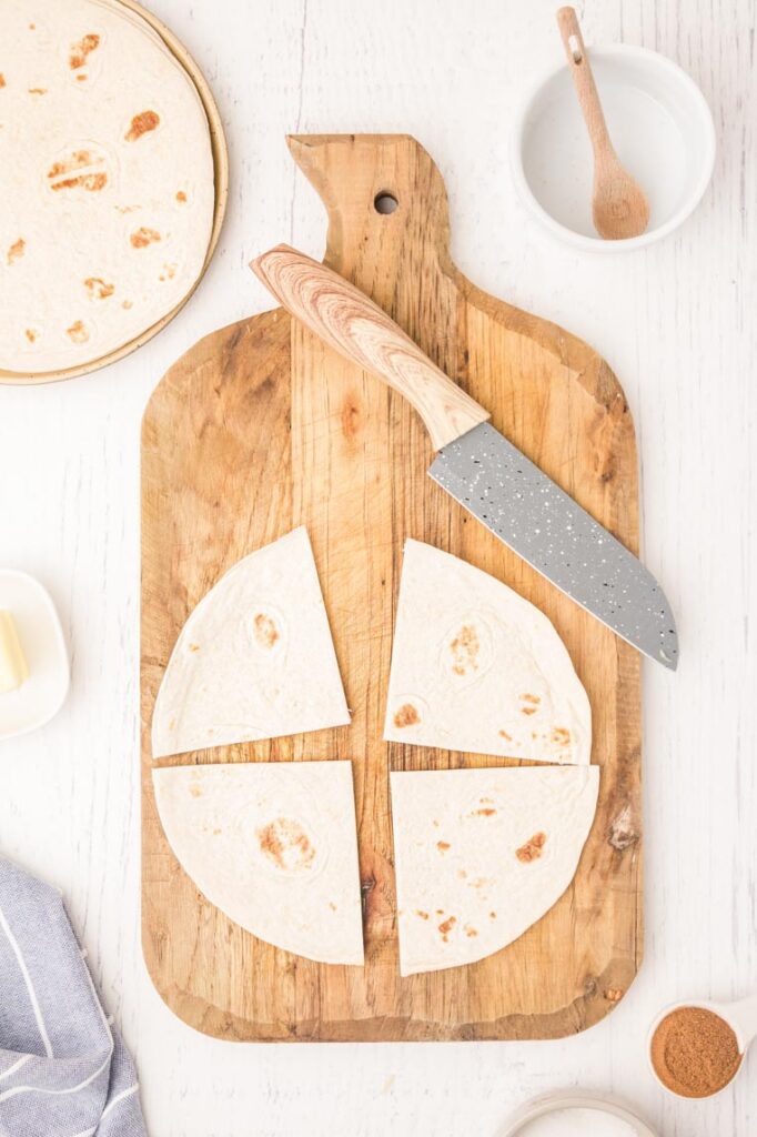 tortillas on a cutting board with a knife cutting tortillas in to quarters
