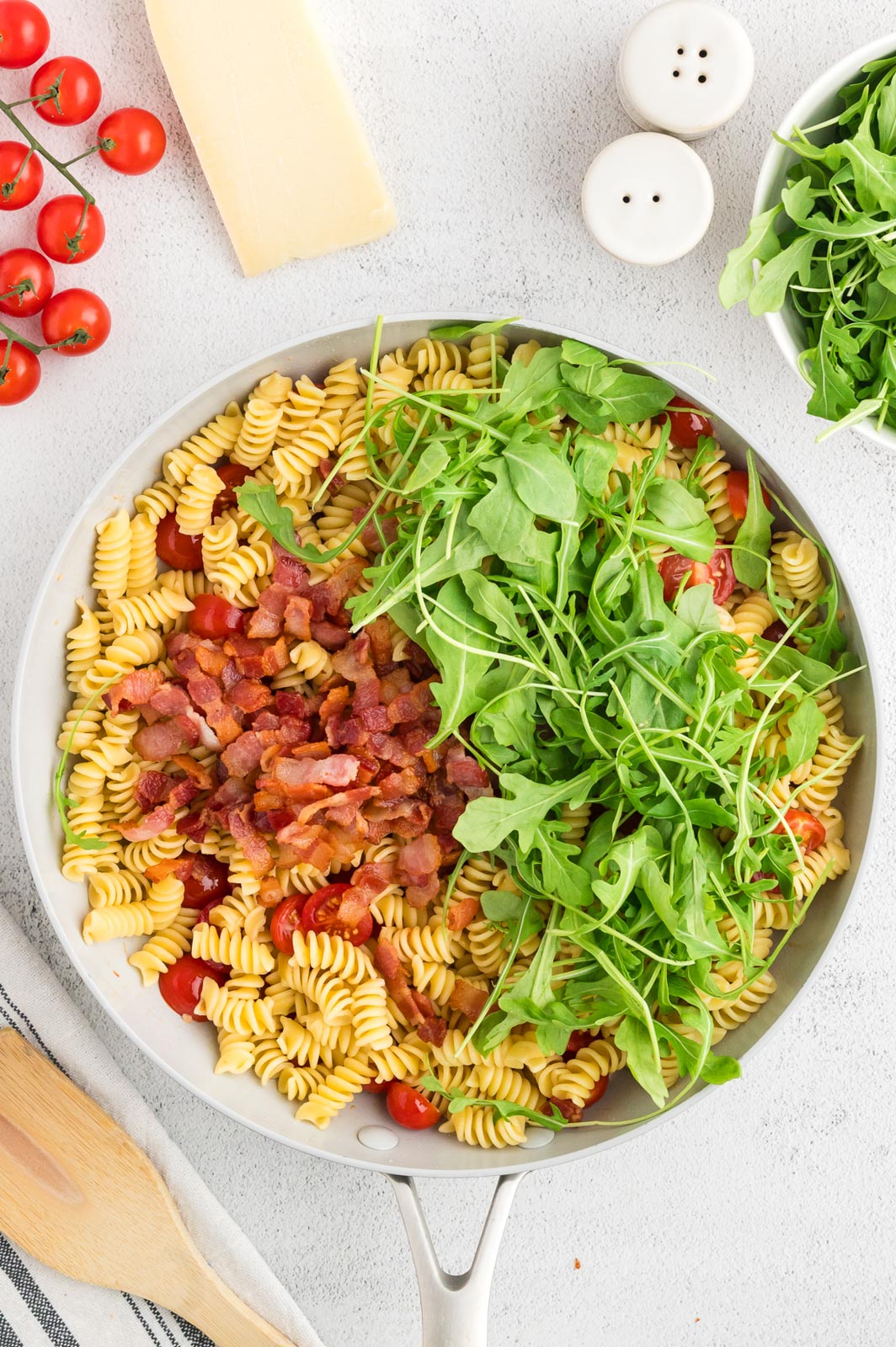 a skillet with fresh arugula added to pasta and cooked bacon 