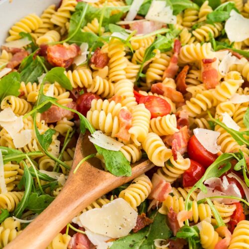 a close up of blt pasta salad in a bowl with a wooden spoon