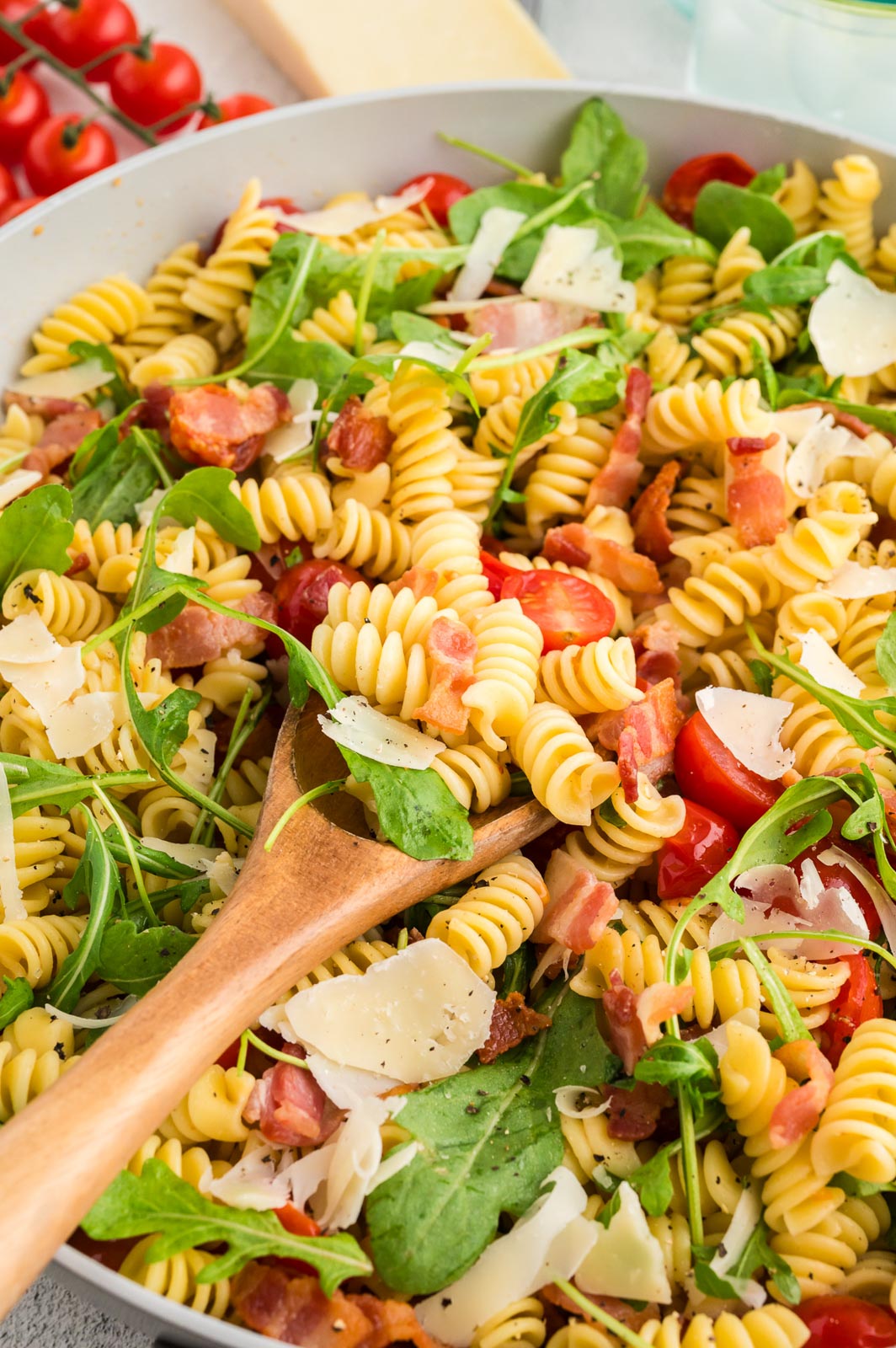 a close up of blt pasta salad in a bowl with a wooden spoon 