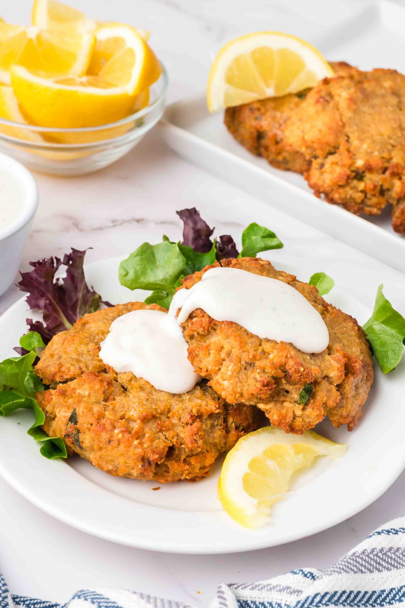 two salmon patties with sour cream and lemons on a plate 