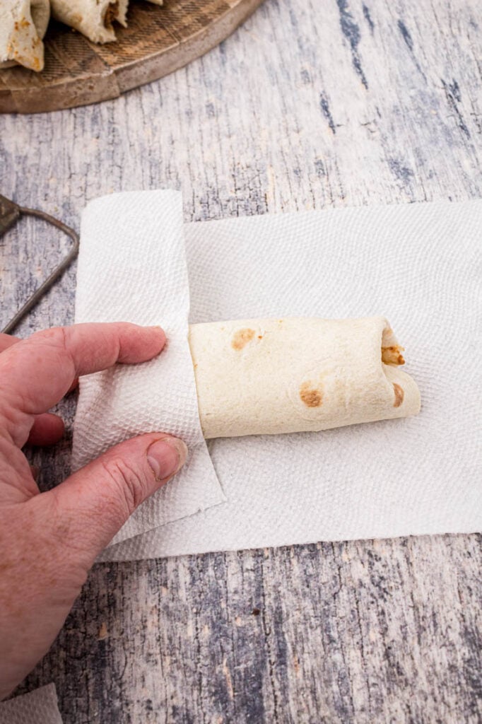 A paper towel with a burrito laid on it and the side folded over a demonstration of how to wrap the burrito in the paper towel. 