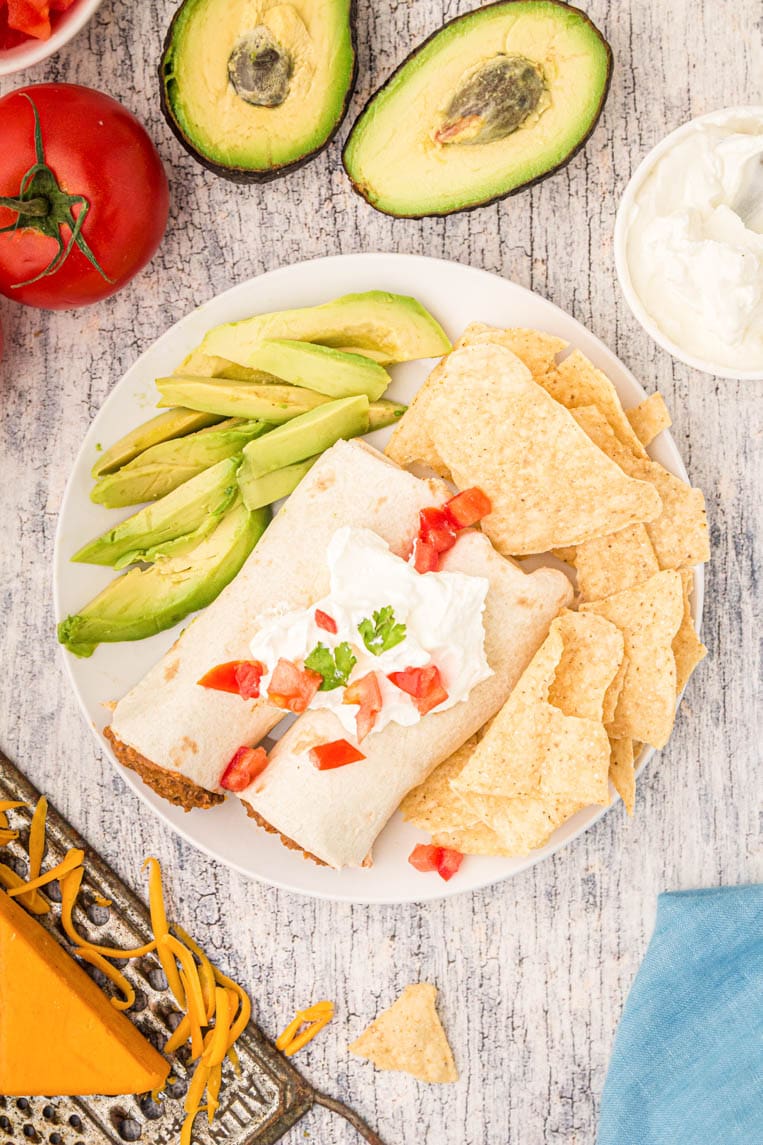 Two burritos on a plate with sour cream and avocado 