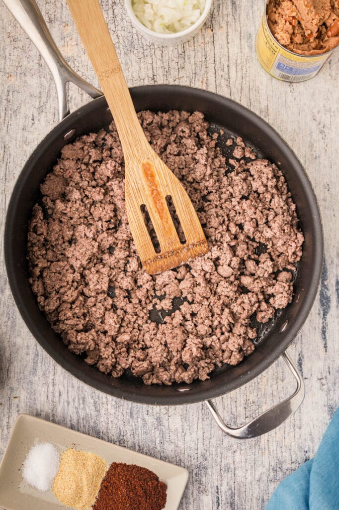 A skillet with browned ground beef and a spoon 