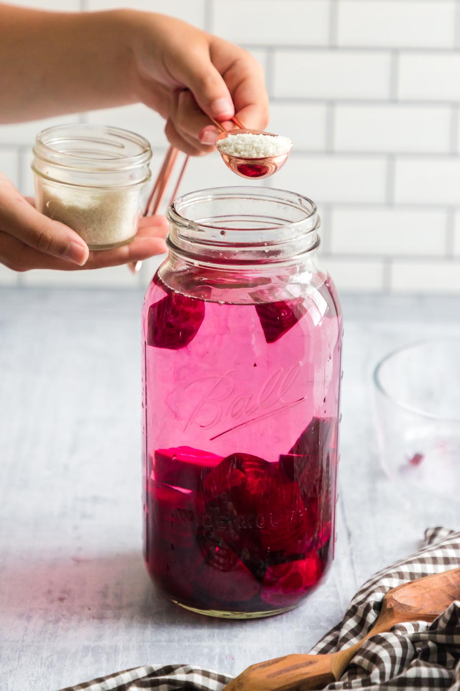 a jar of beets and water with a tablespoon of salt being added