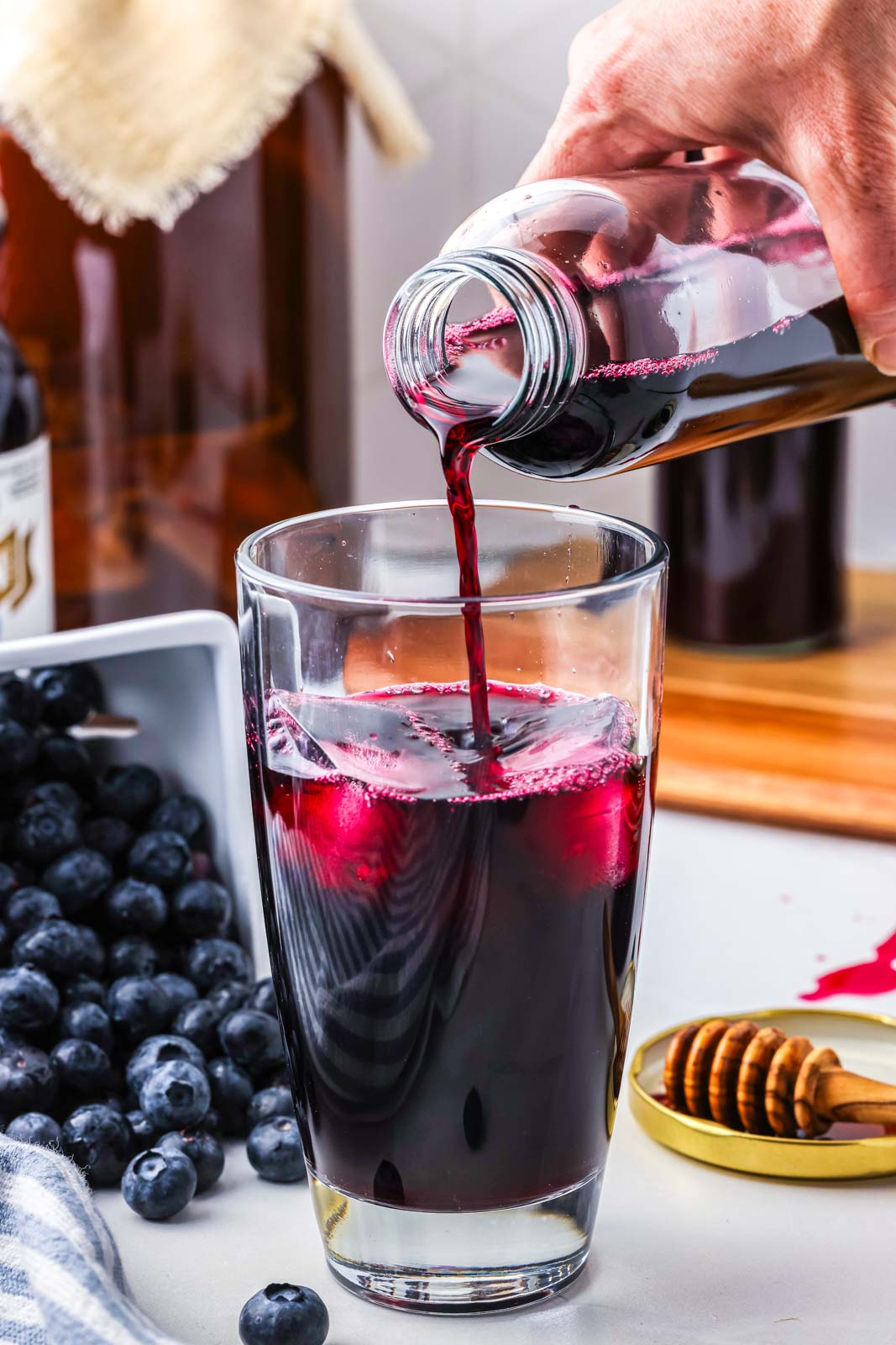 a cup being filled with blueberry kombucha being poured from a narrow jar