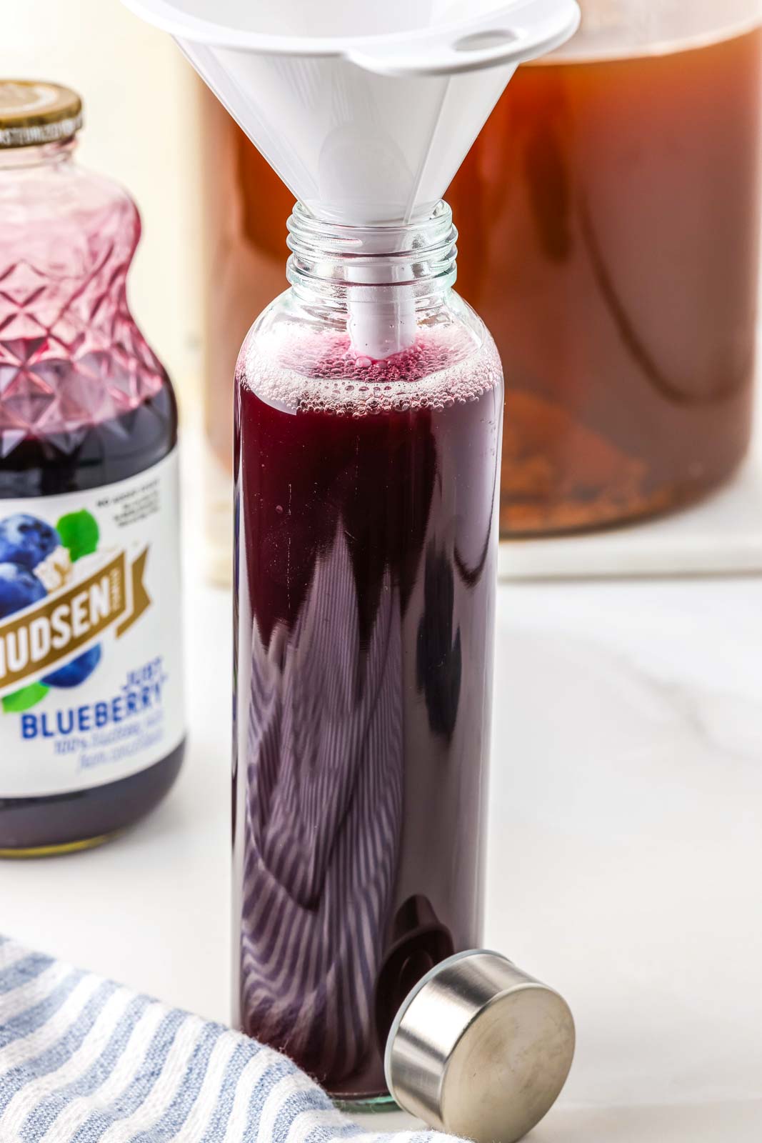 a glass bottle being filled with kombucha and blueberry juice 