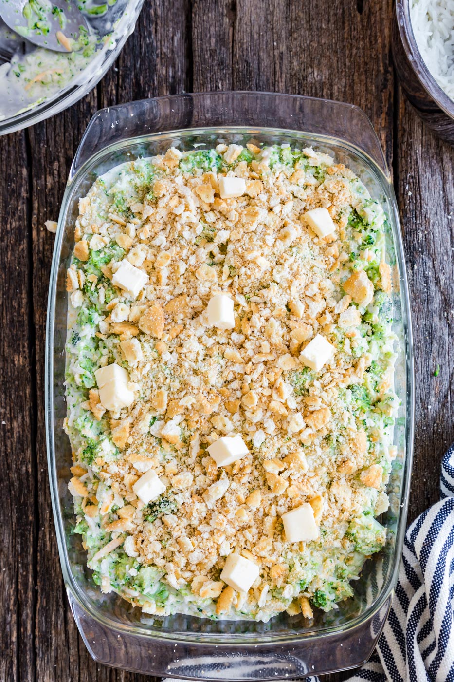 a dish of broccoli cheddar rice casserole on a table with crushed crackers and cold butter 