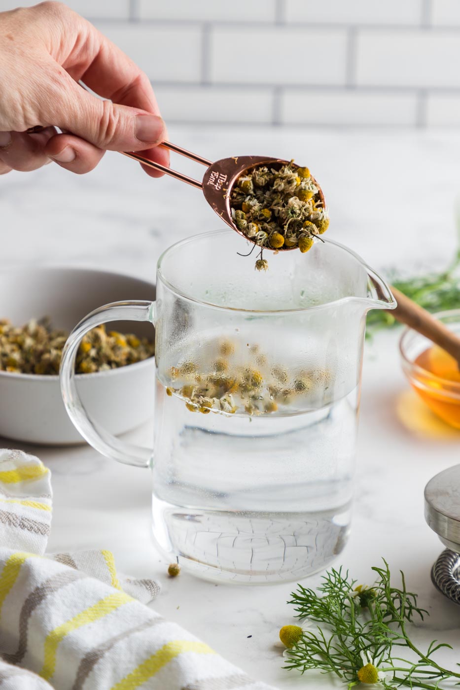 a spoon adding dried chamomile flowers to hot water