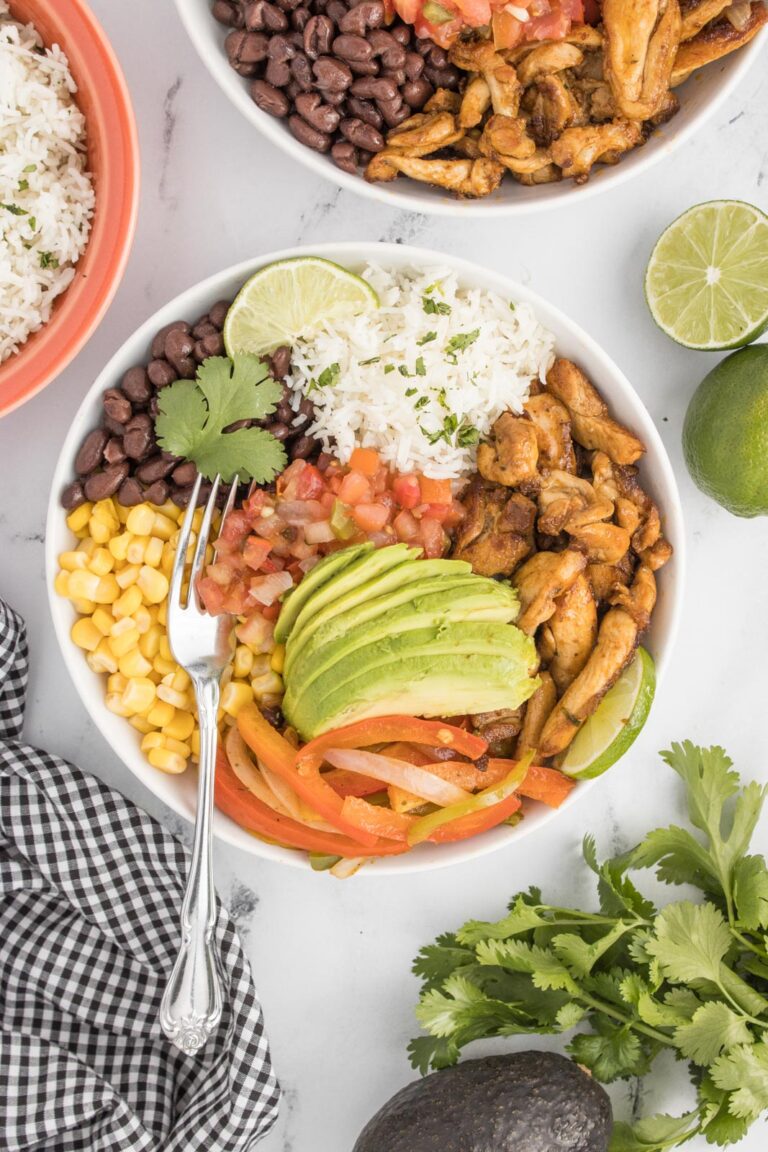 a chicken fajita bowl on a table and piled high with avocado, salsa, corn, beans, cilantro and rice