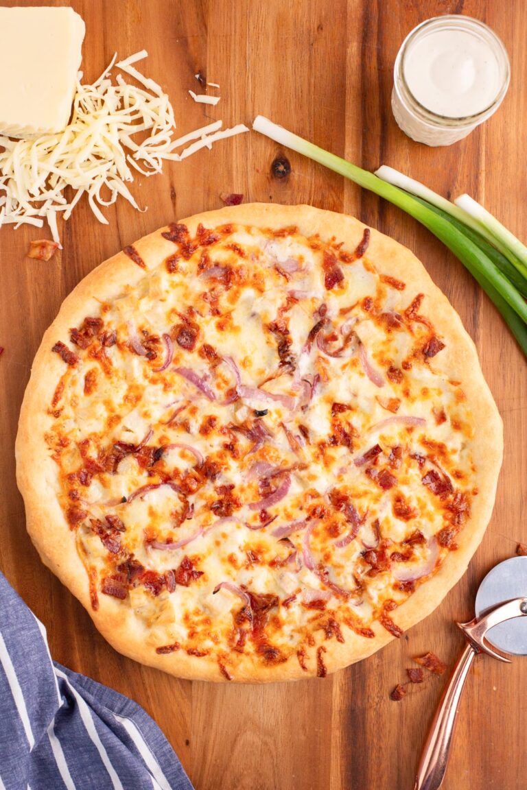 Overehead image of chicken bacon ranch pizza on a wooden work surface near cheese, scallions, and ranch dressing.