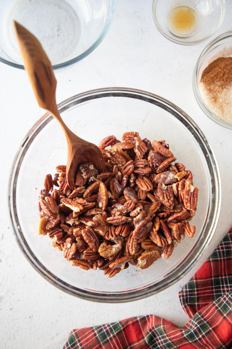 a bowl of pecans with a spoon that have been tossed with egg whites