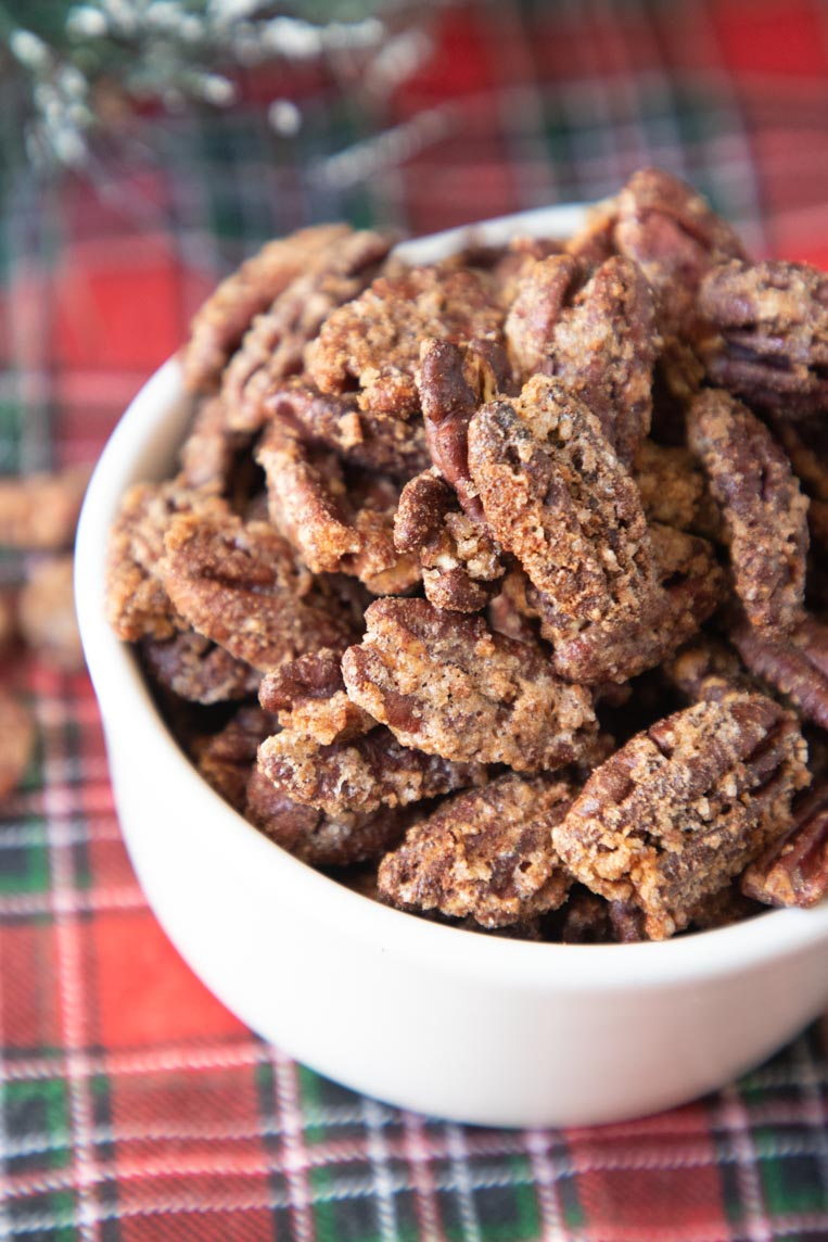 an up close photo of candied pecans in a white bowl on a holiday table