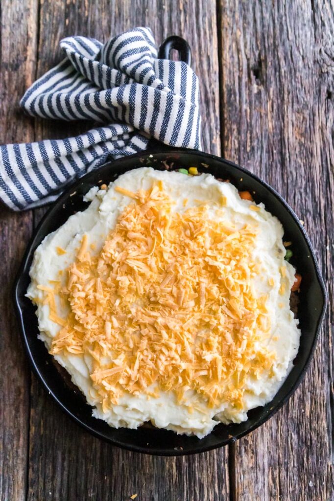a skillet of cottage pie with cheese on top ready to bake 