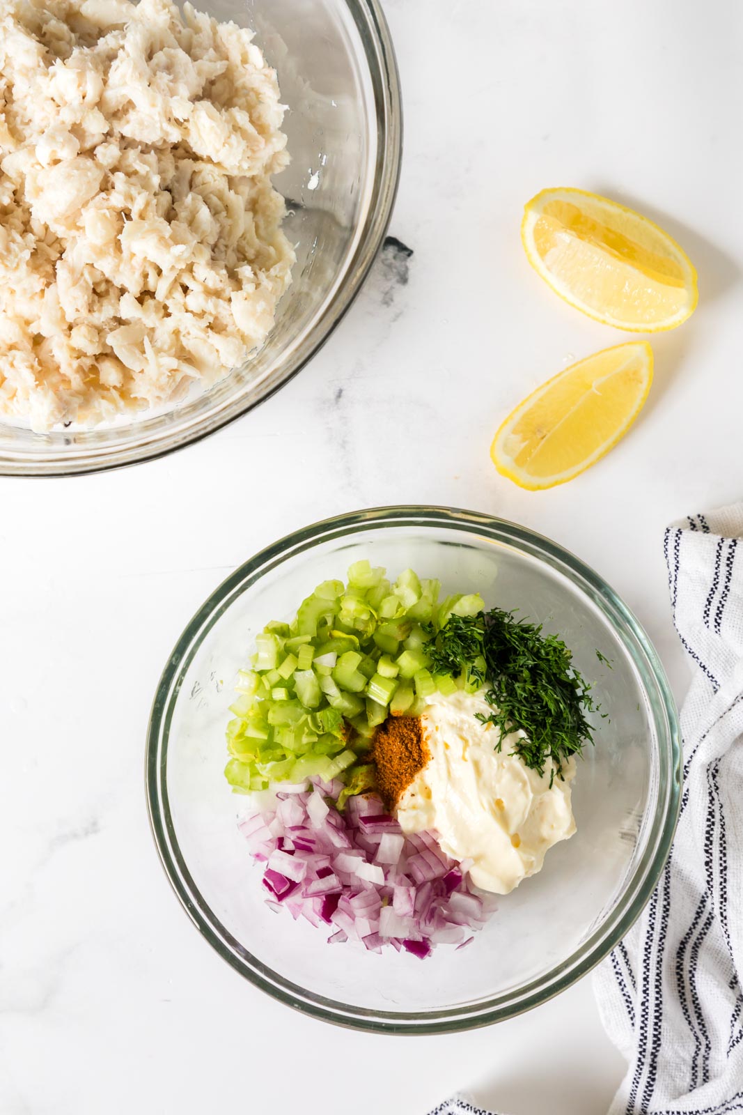 Overhead image of a bowl of lump crab meat next to a bowl full of the remaining ingredients for crab meat salad.