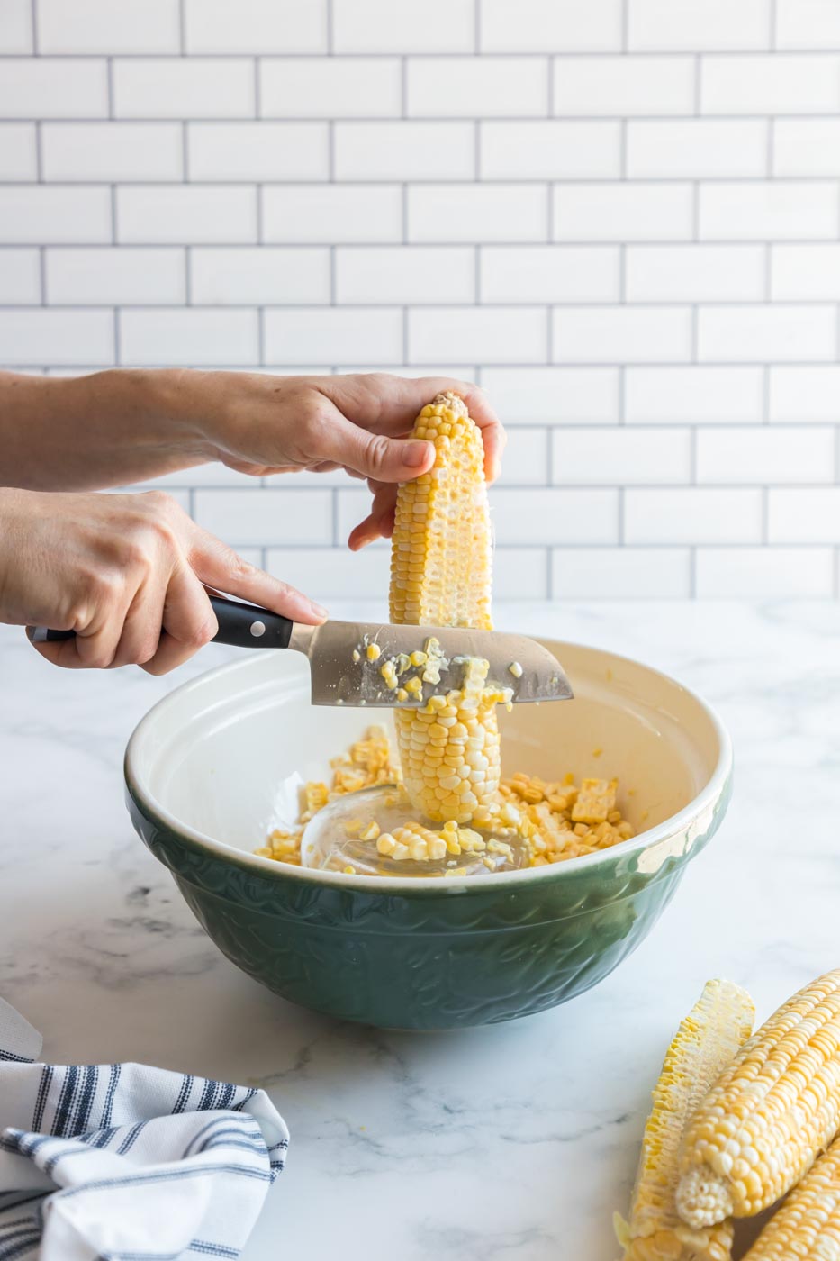using knife to scrape kernels of corn cob into a bowl