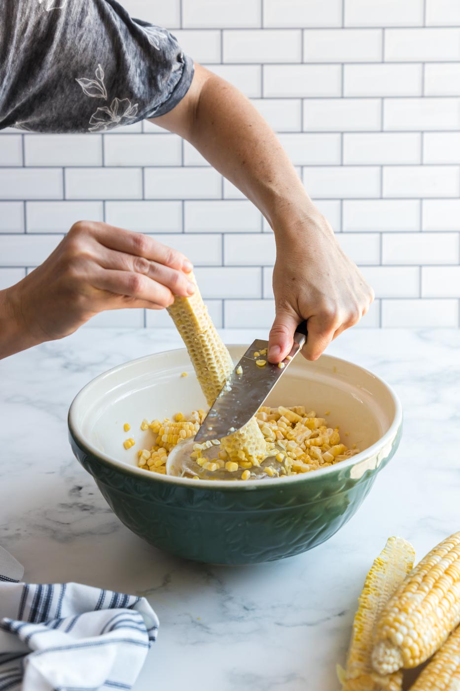 using back of knife to scrape starchy liquid off corn cob into bowl to make creamed corn