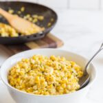 white bowl of creamed corn with skillet in background