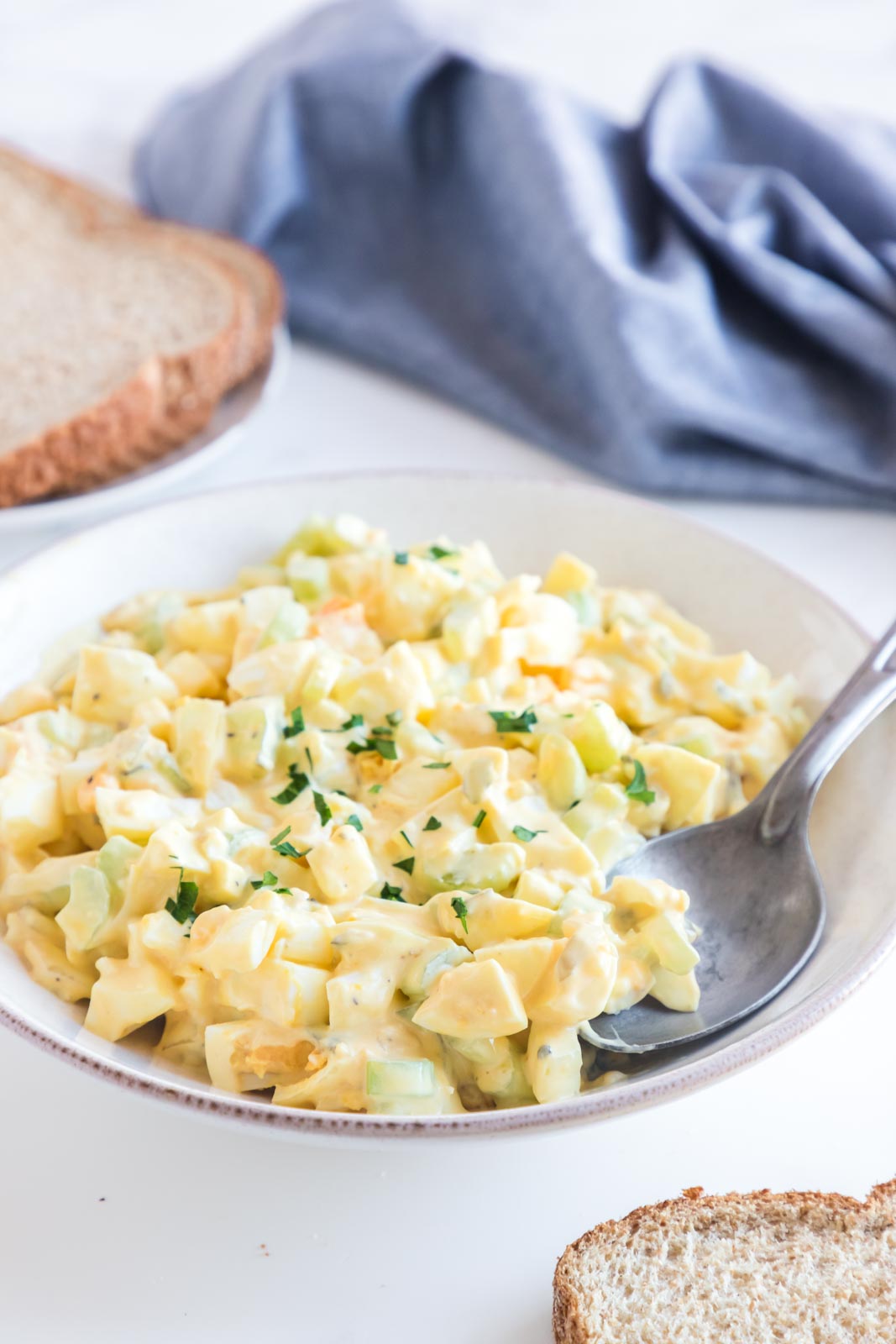 a bowl of egg salad on a table with a spoon and a napkin 