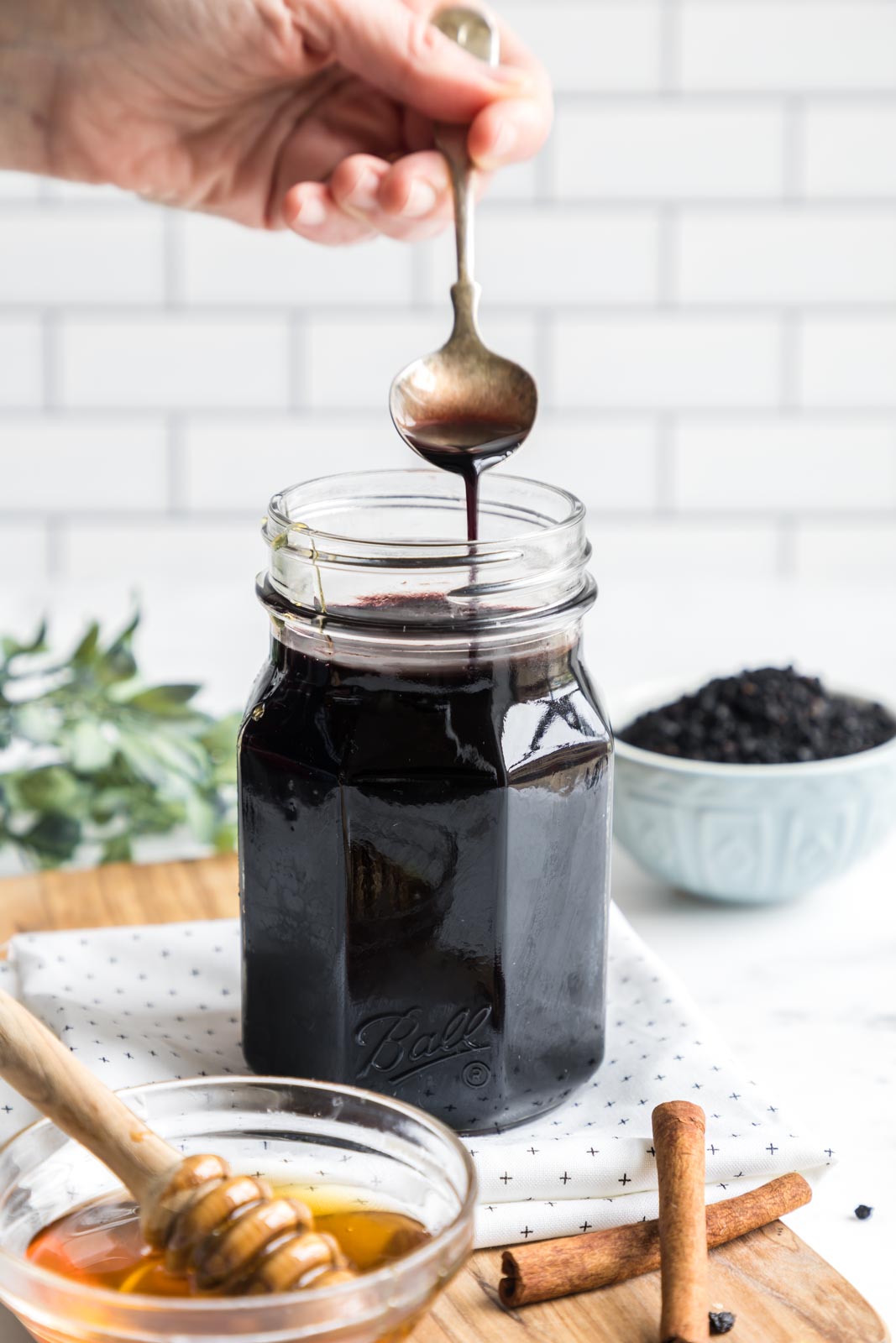 a jar of elderberry syrup with a spoon pouring out 