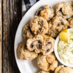 Fried mushrooms on a plate with a bowl of dipping sauce.