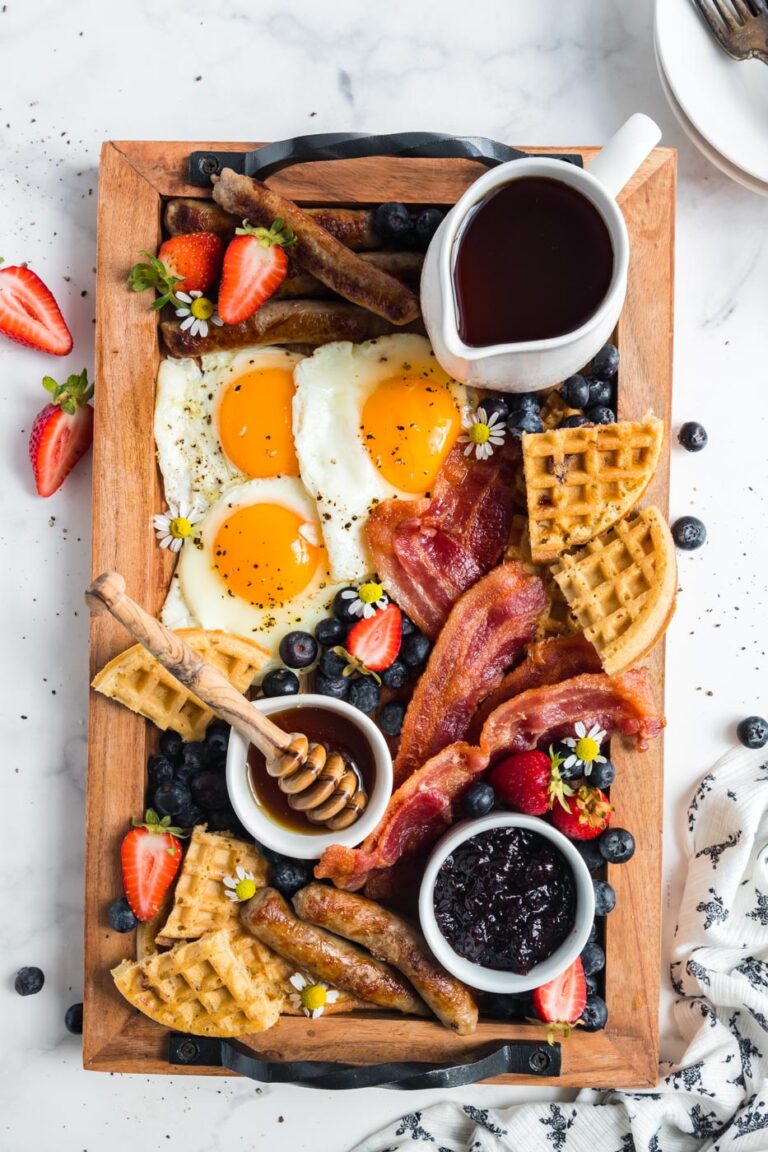 breakfast charcuterie board filled with eggs bacon waffles sausage fruit syrup honey