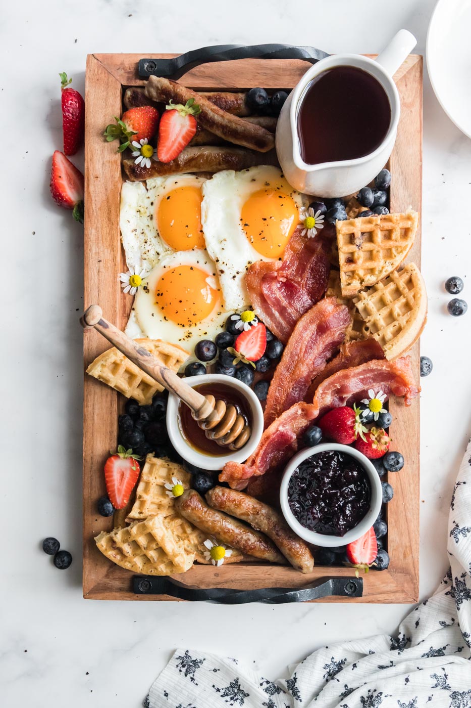 healthy breakfast charcuterie board with eggs sausage links bacon waffles fruit jam syrup honey