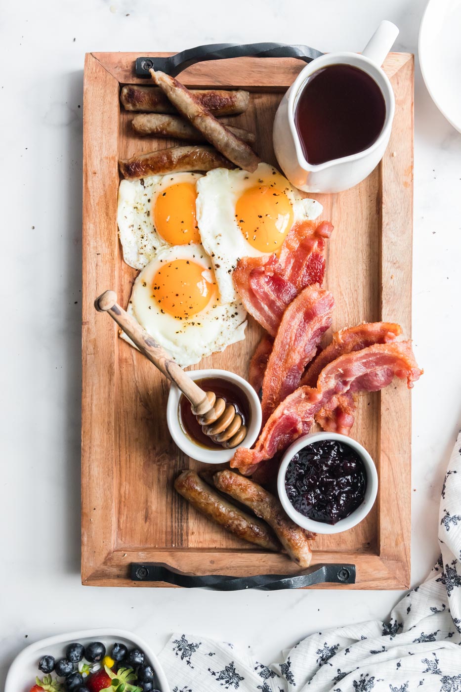 jars of honey maple syrup sunny side up eggs bacon and sausage links arranged on breakfast charcuterie board