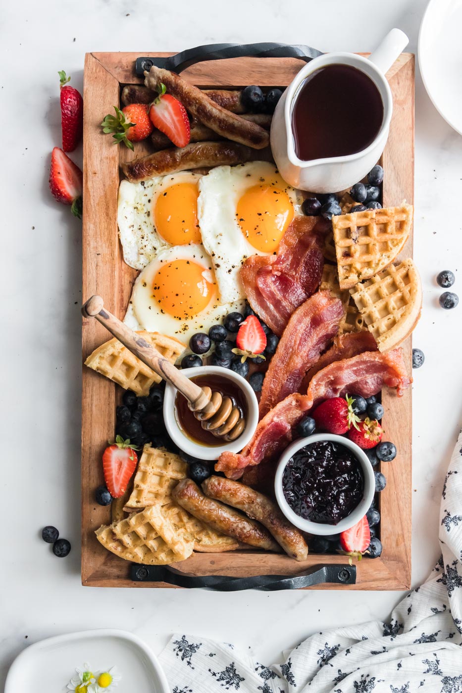 healthy breakfast charcuterie board with eggs sausage links bacon waffles fruit pot of jam pitcher of syrup honey