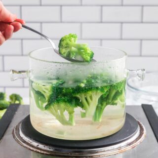 a pot of broccoli being blanched with a spoon holding a piece of broccoli over the top of the pot