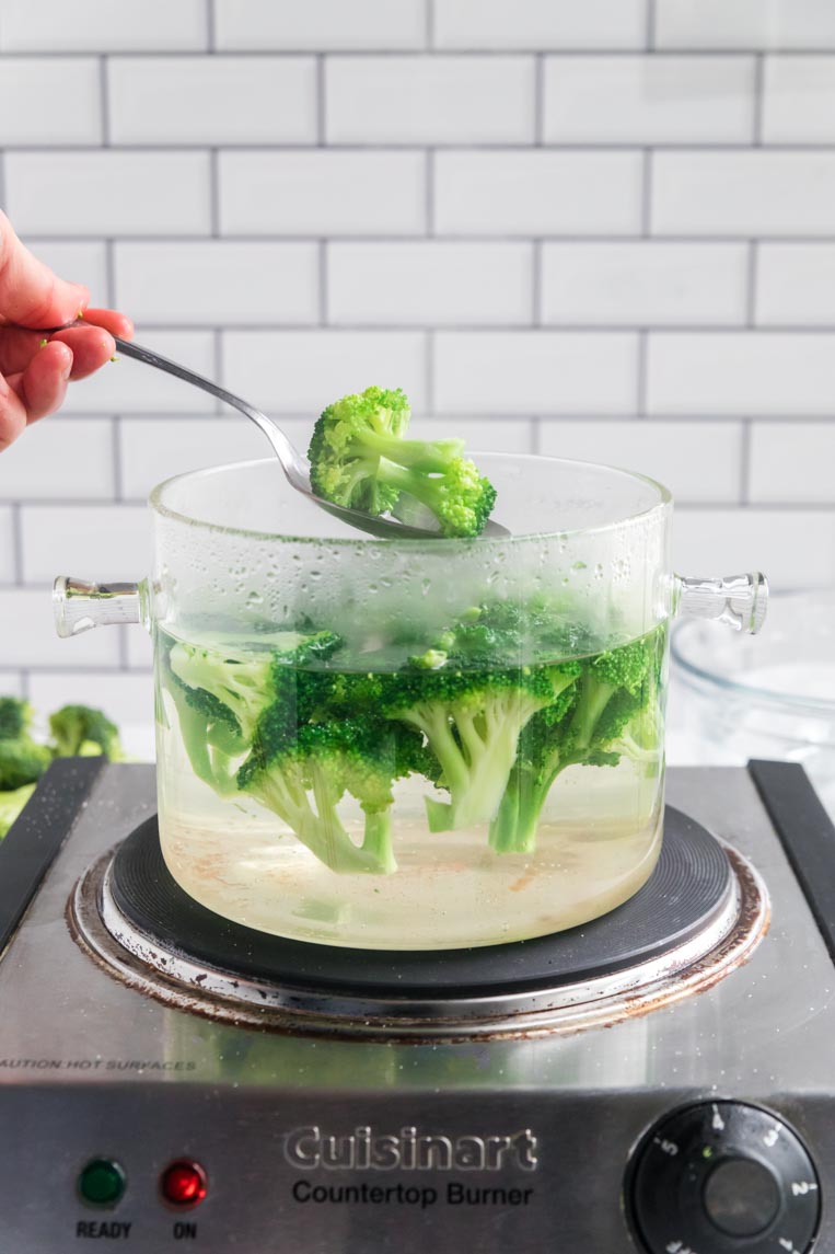 a pot of broccoli being blanched with a spoon holding a piece of broccoli over the top of the pot
