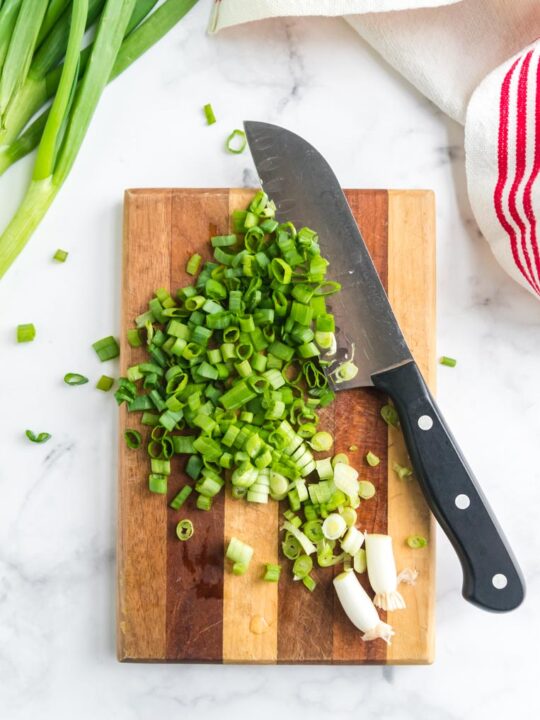 a cutting board with chopped green onions and a knife