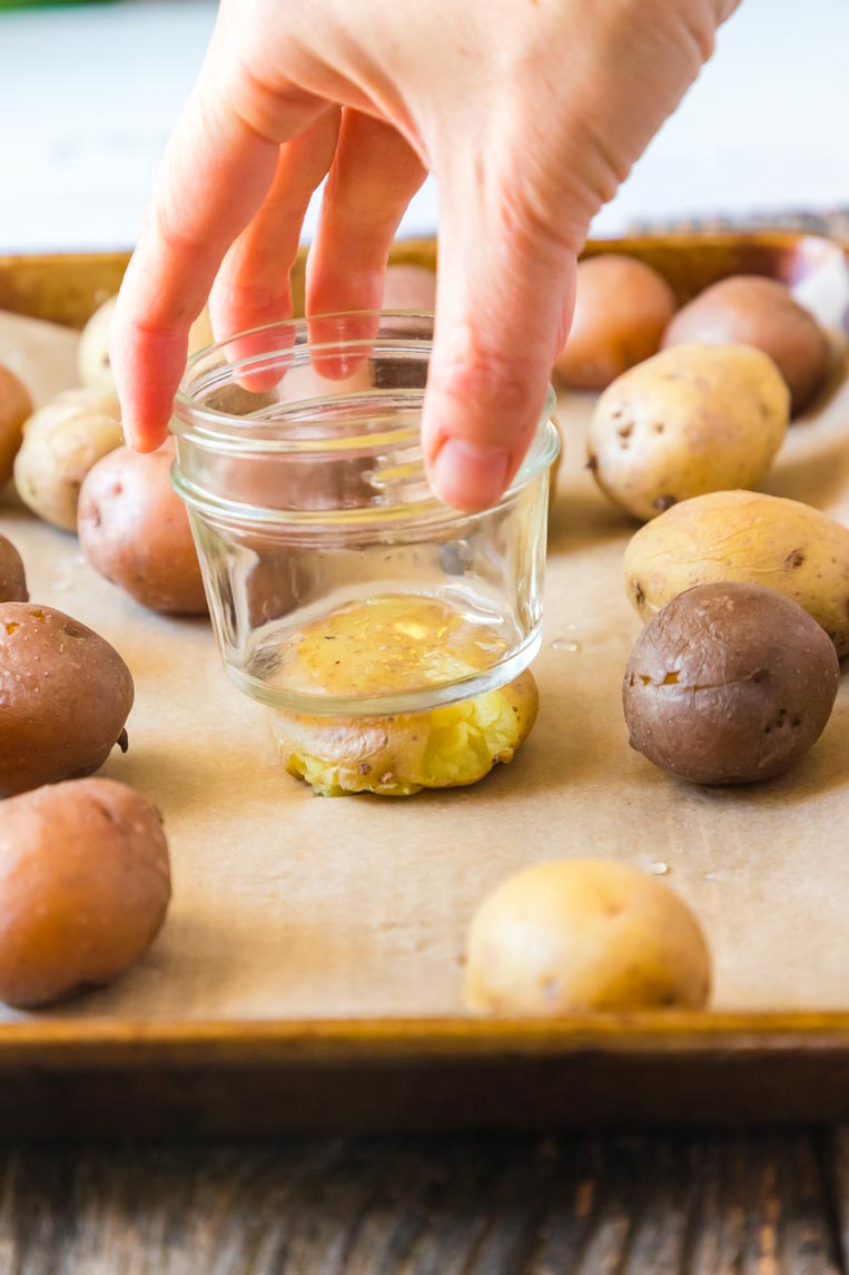 a hand pressing down on steamed potatoes on a baking tray 