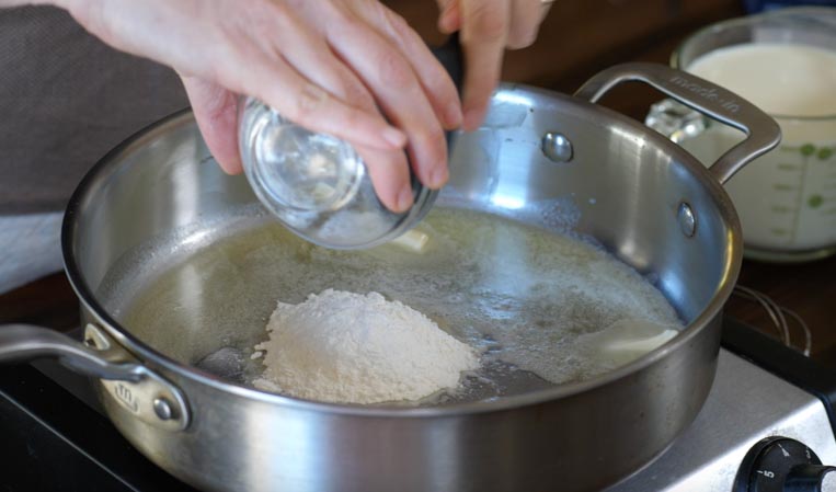 flour being added to a pan of melted butter 
