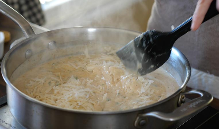 cheese being stirred into a pot of bechamel with a spatula